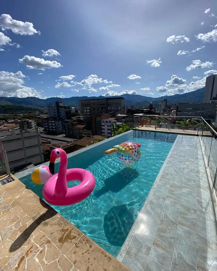 Piscina de la azotea de Appartments Hotel un día soleado, con flotadores en el agua y la ciudad al fondo